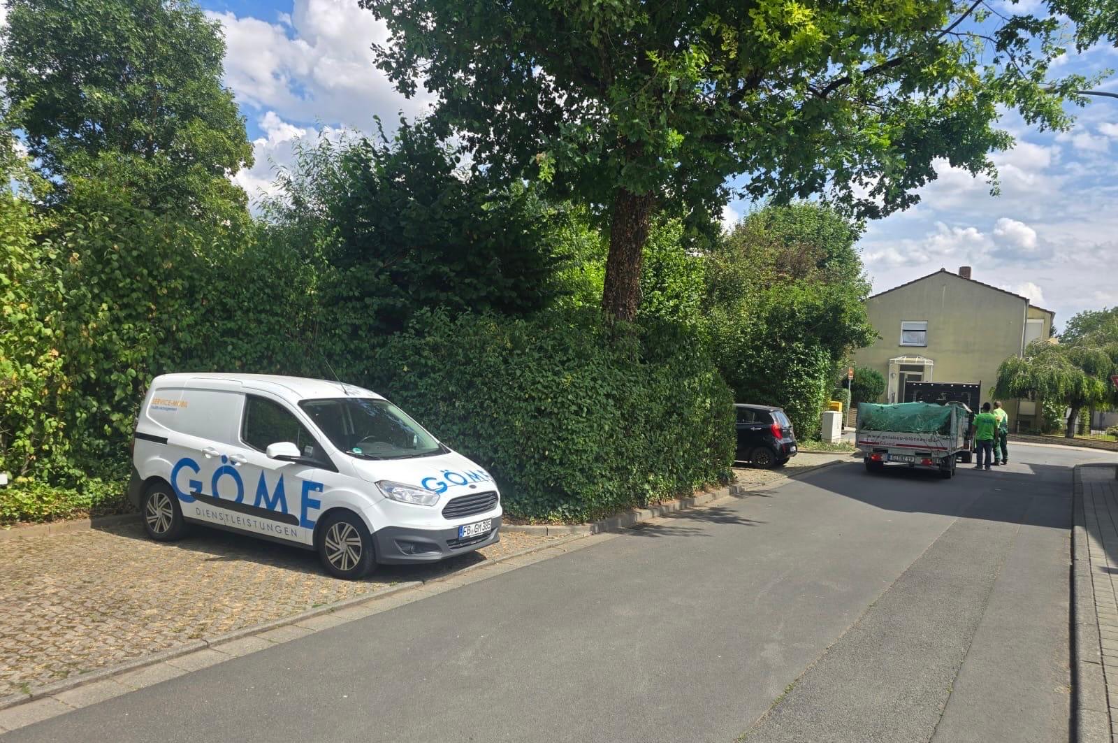 GÖME-Fahrzeug vor einer gepflegten Hecke, Mitarbeiter im Hintergrund beim Verladen