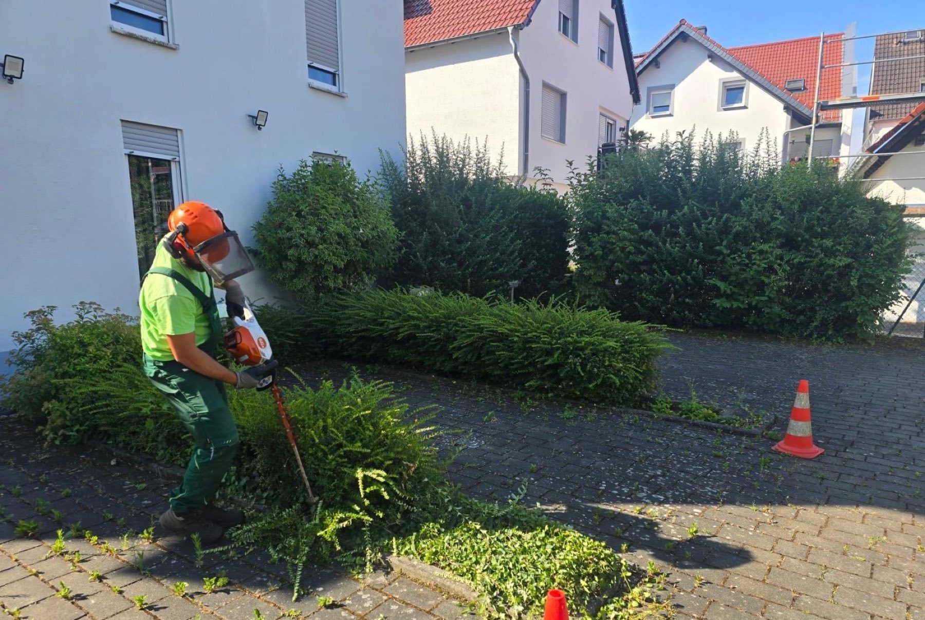 Mitarbeiter mit voller Schutzausrüstung beim Heckenschnitt